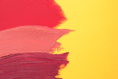 Smears of different beautiful lipsticks on yellow background, top view. Space for text
