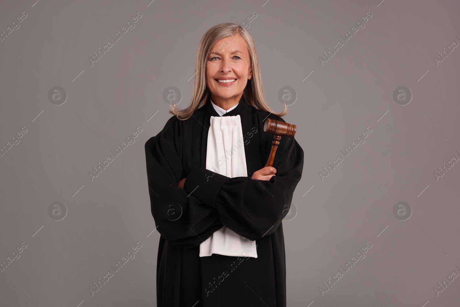 Photo of Smiling senior judge with gavel on grey background