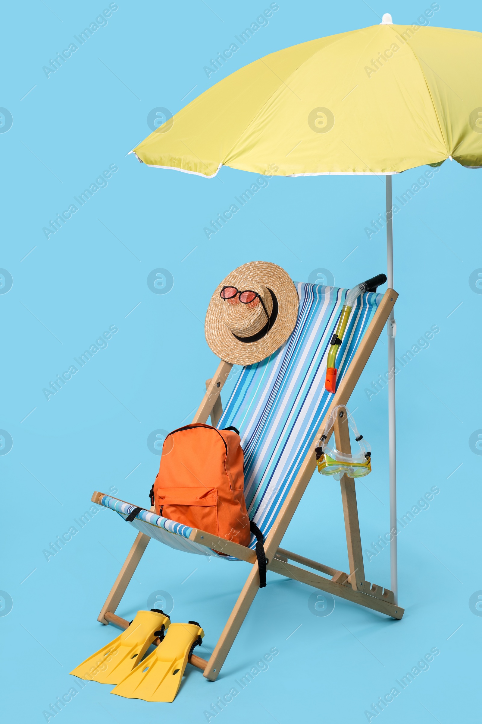 Deck chair, backpack and beach accessories on light blue background Photo of Deck chair, backpack and beach accessories on light blue background