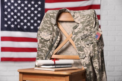 Photo of Chair with soldier uniform, notebooks and diploma near flag of United States indoors. Military education