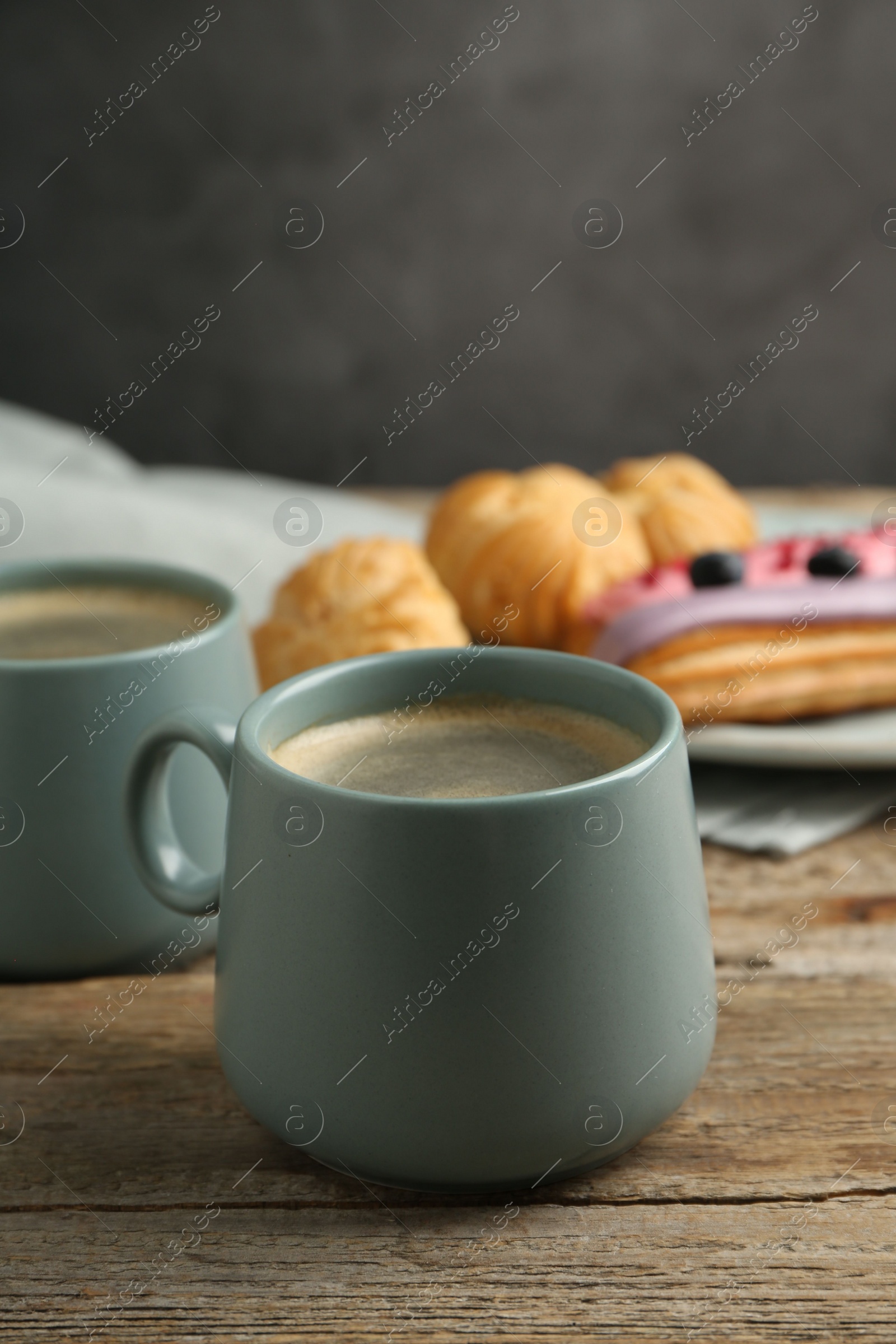 Photo of Aromatic coffee in cups, tasty eclairs and profiteroles on wooden table