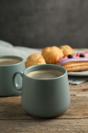 Aromatic coffee in cups, tasty eclairs and profiteroles on wooden table