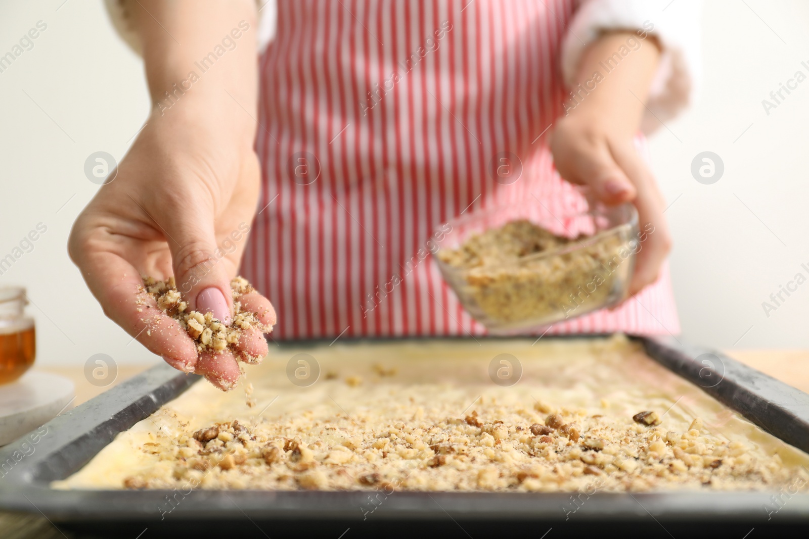 Photo of Making delicious baklava. Woman adding chopped nuts to dough at table, closeup