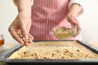 Making delicious baklava. Woman adding chopped nuts to dough at table, closeup