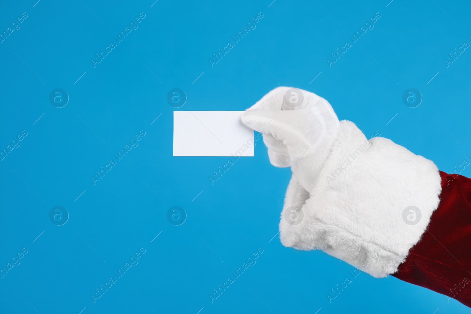 Photo of Santa Claus holding blank card on blue background, closeup of hand. Space for text