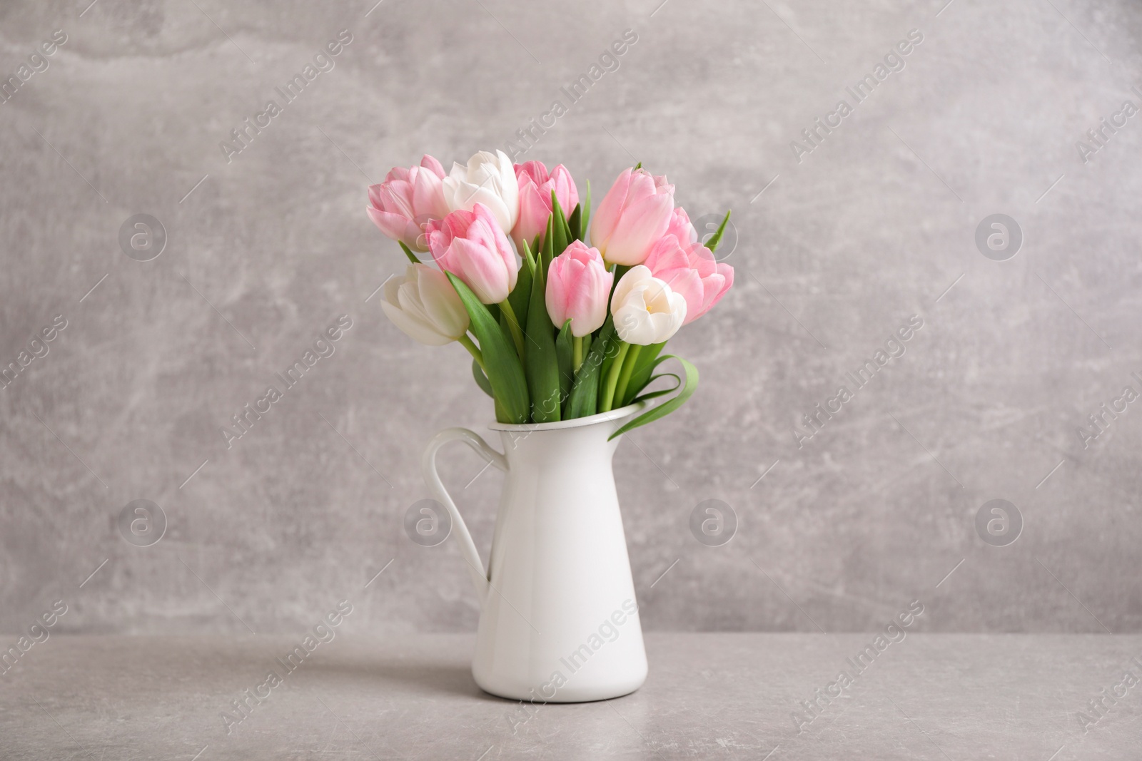 Photo of Beautiful bouquet of tulips in jug on light table