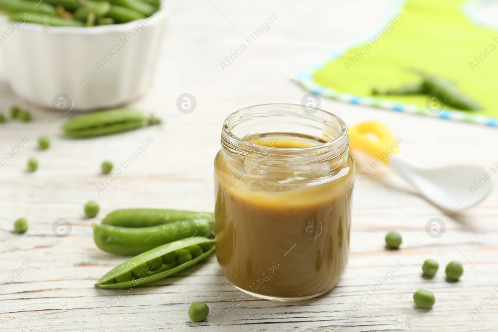 Photo of Jar with healthy baby food and green peas on table