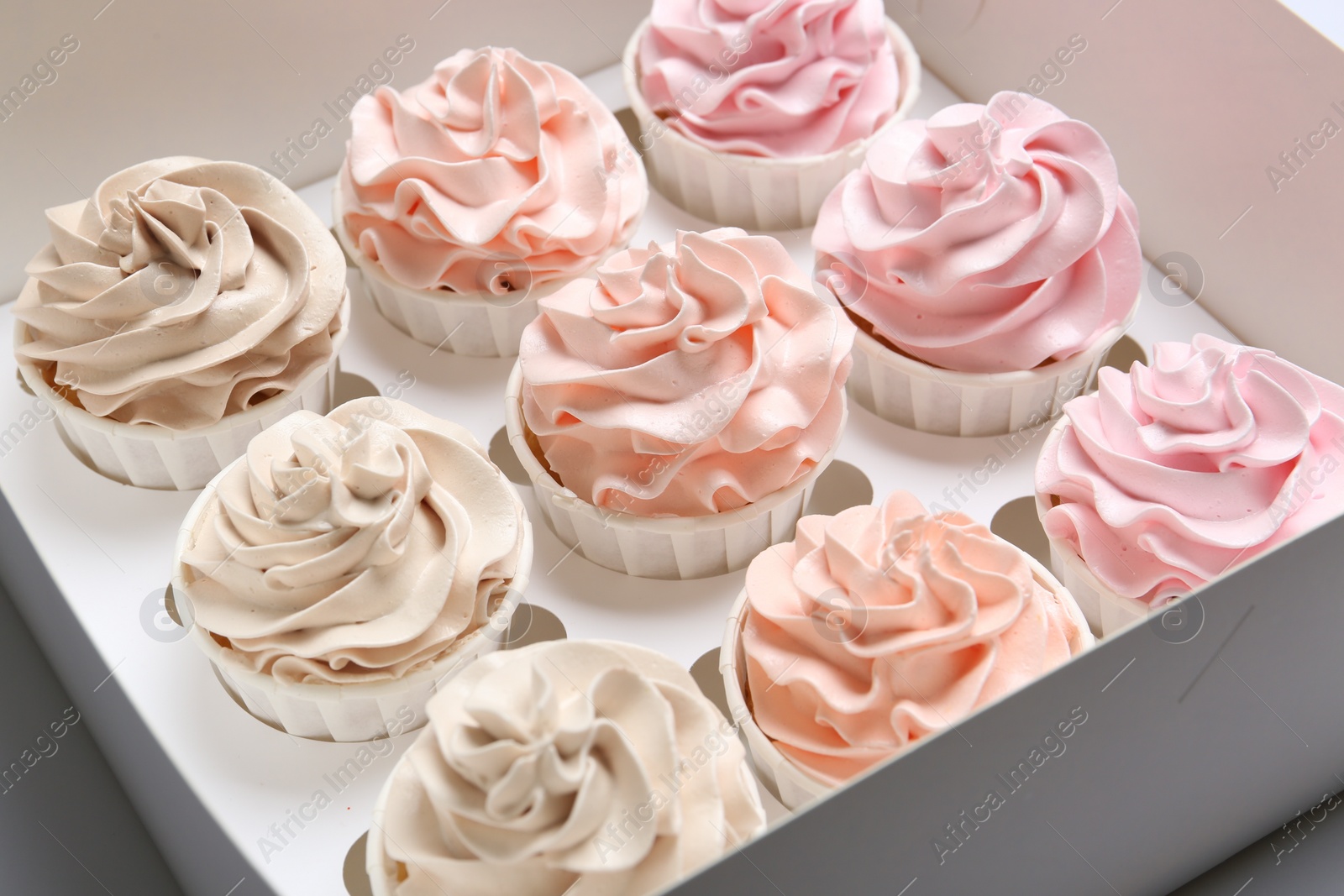 Photo of Many tasty cupcakes with colorful cream in box, closeup