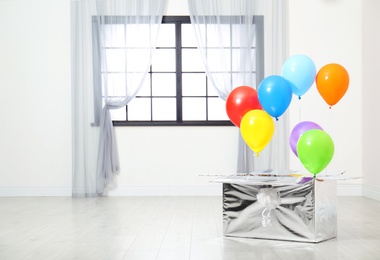 Gift box with bright air balloons on floor indoors. Space for text