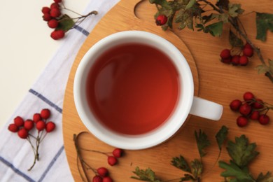 Cup with hawthorn tea and berries on beige table, flat lay