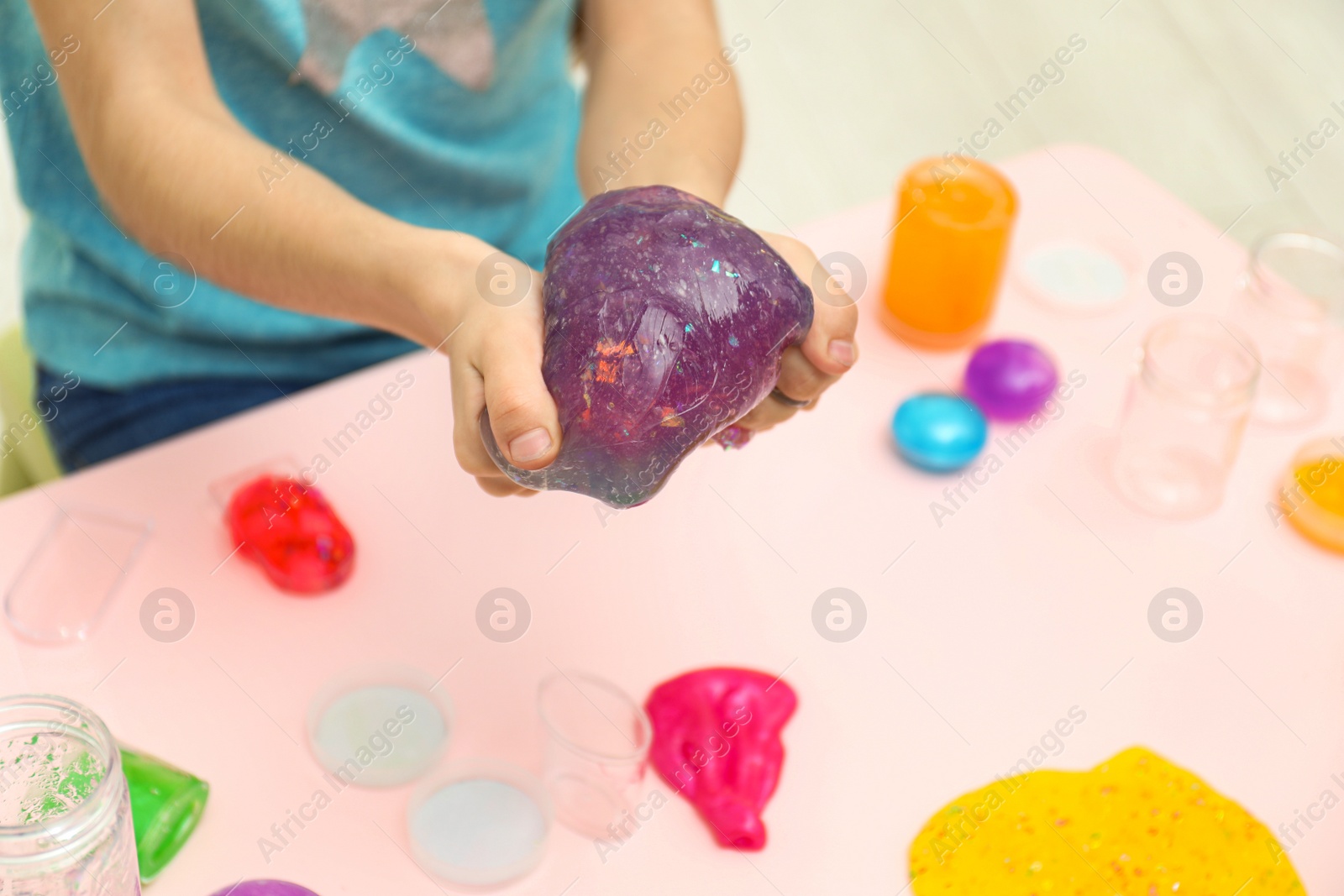 Photo of Girl holding purple slime over table, closeup