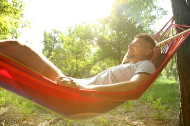 Young man resting in comfortable hammock at green garden