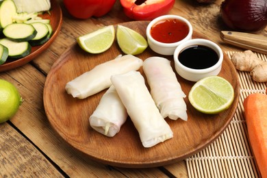 Photo of Delicious spring rolls with vegetables, lime and sauces on wooden table, closeup