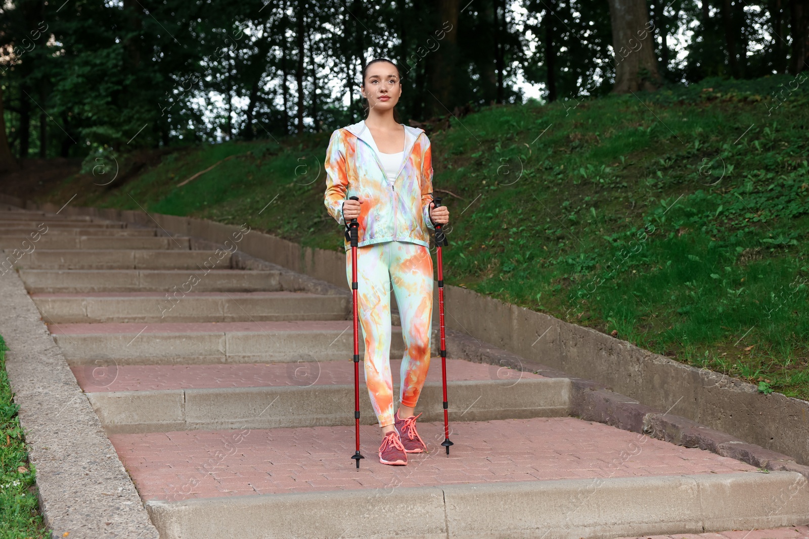 Photo of Young woman practicing Nordic walking with poles on steps outdoors