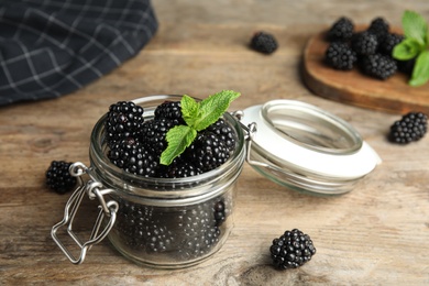 Photo of Glass jar of tasty blackberries and mint on wooden table