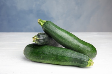 Photo of Fresh ripe green zucchinis on white wooden table against blue background