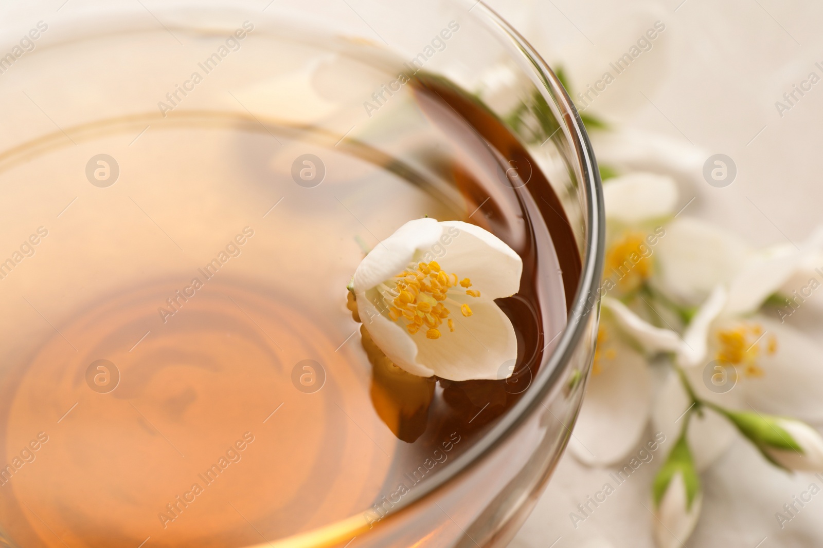 Photo of Glass cup of aromatic jasmine tea and fresh flowers, closeup