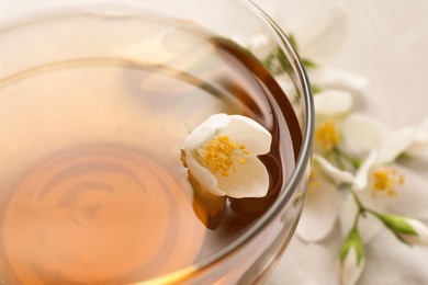 Photo of Glass cup of aromatic jasmine tea and fresh flowers, closeup