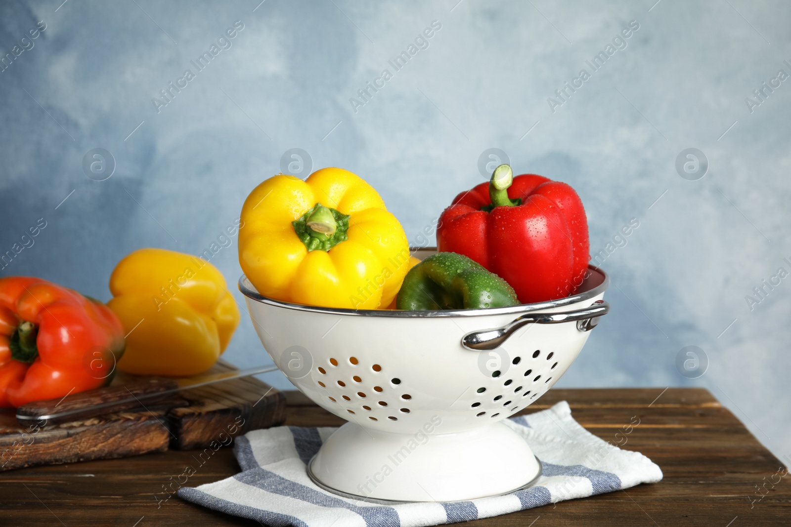 Photo of Colander with ripe paprika peppers on wooden table