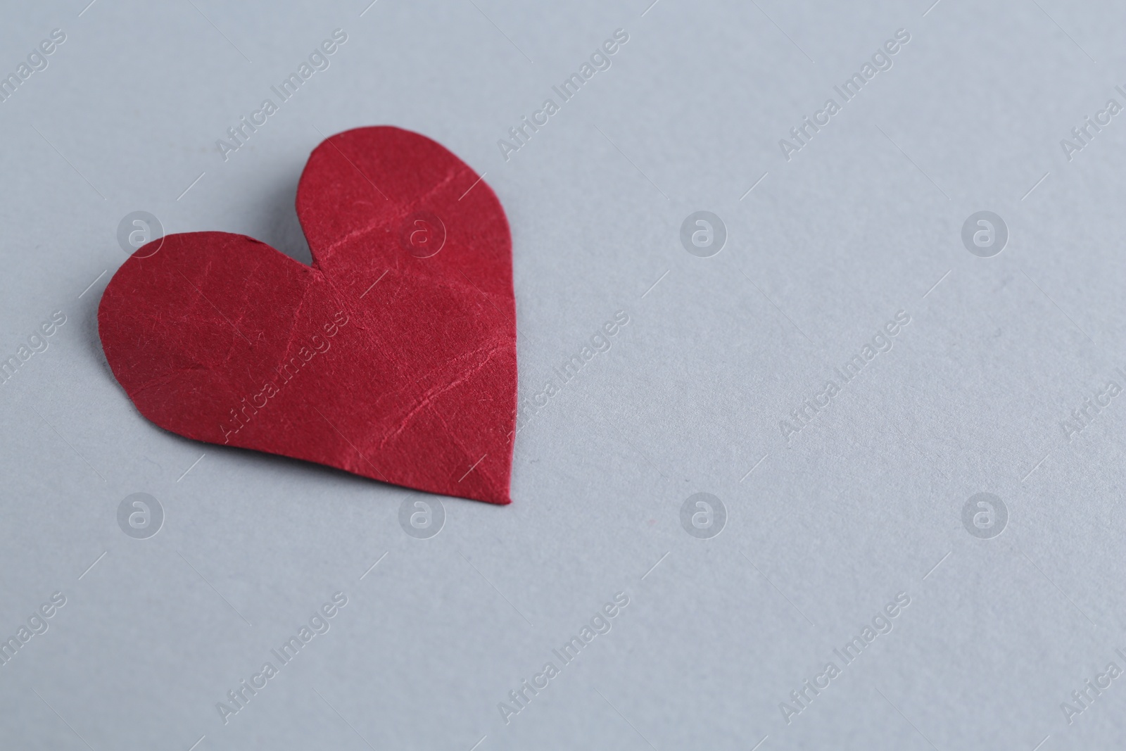 Photo of Red crumpled paper heart on gray background, space for text