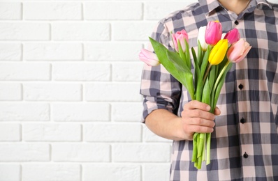 Man holding bouquet of beautiful spring tulips near brick wall, closeup with space for text. International Women's Day