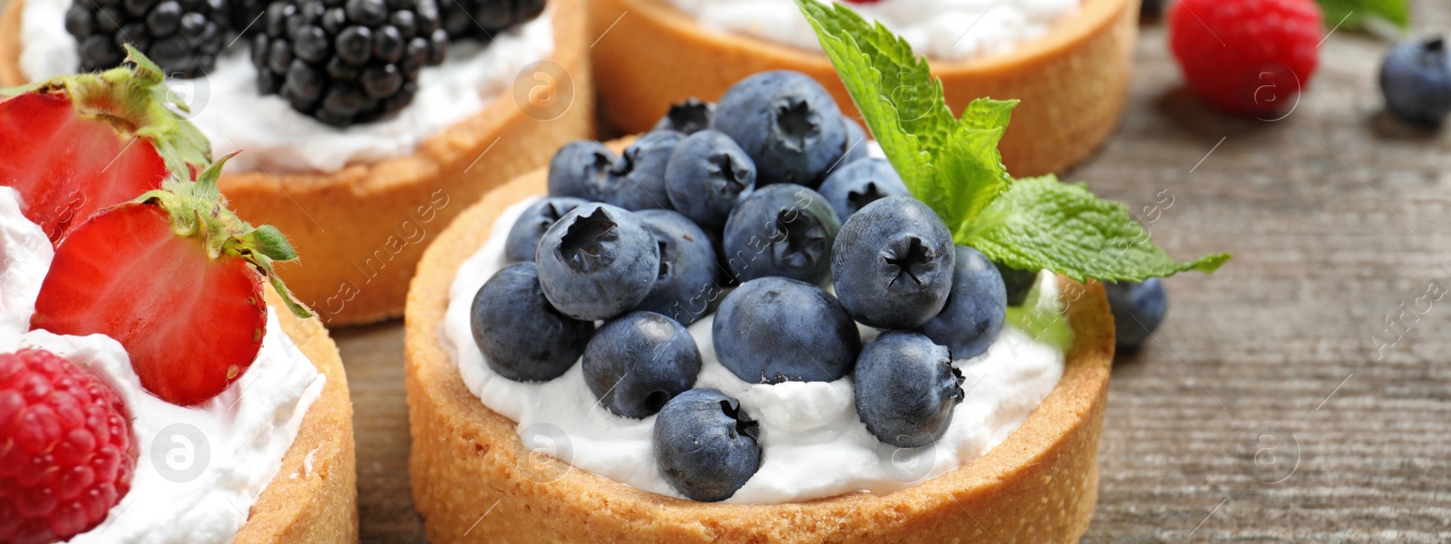 Image of Delicious tartlets with fresh berries on wooden table, closeup. Banner design