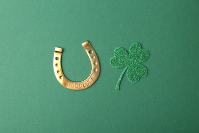 Photo of St. Patrick's day. Golden horseshoe and decorative clover leaf on green background, flat lay