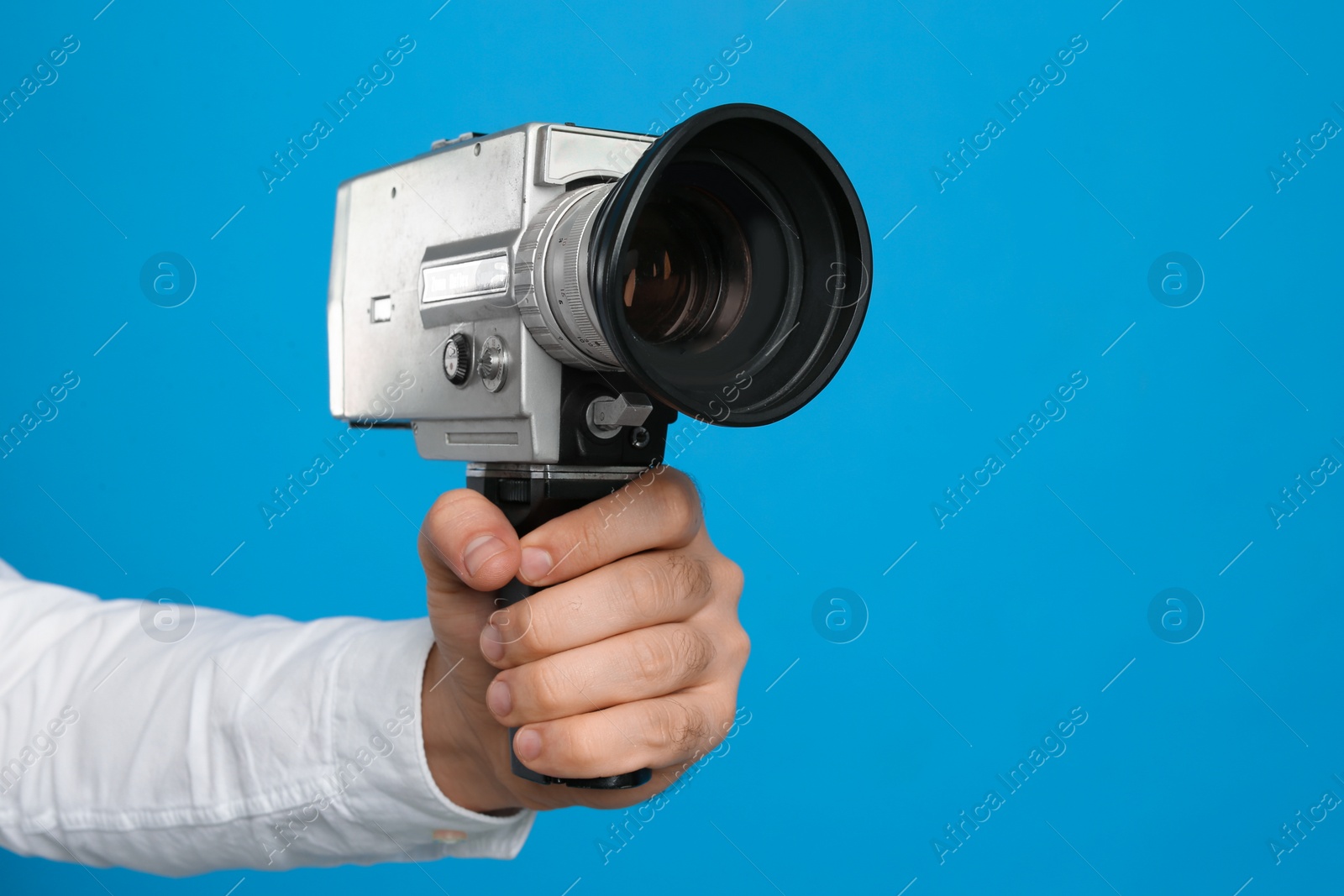 Photo of Man with vintage video camera on light blue background, closeup of hand