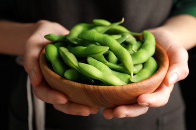 Photo of Woman holding bowl with green edamame beans in pods on black background, closeup