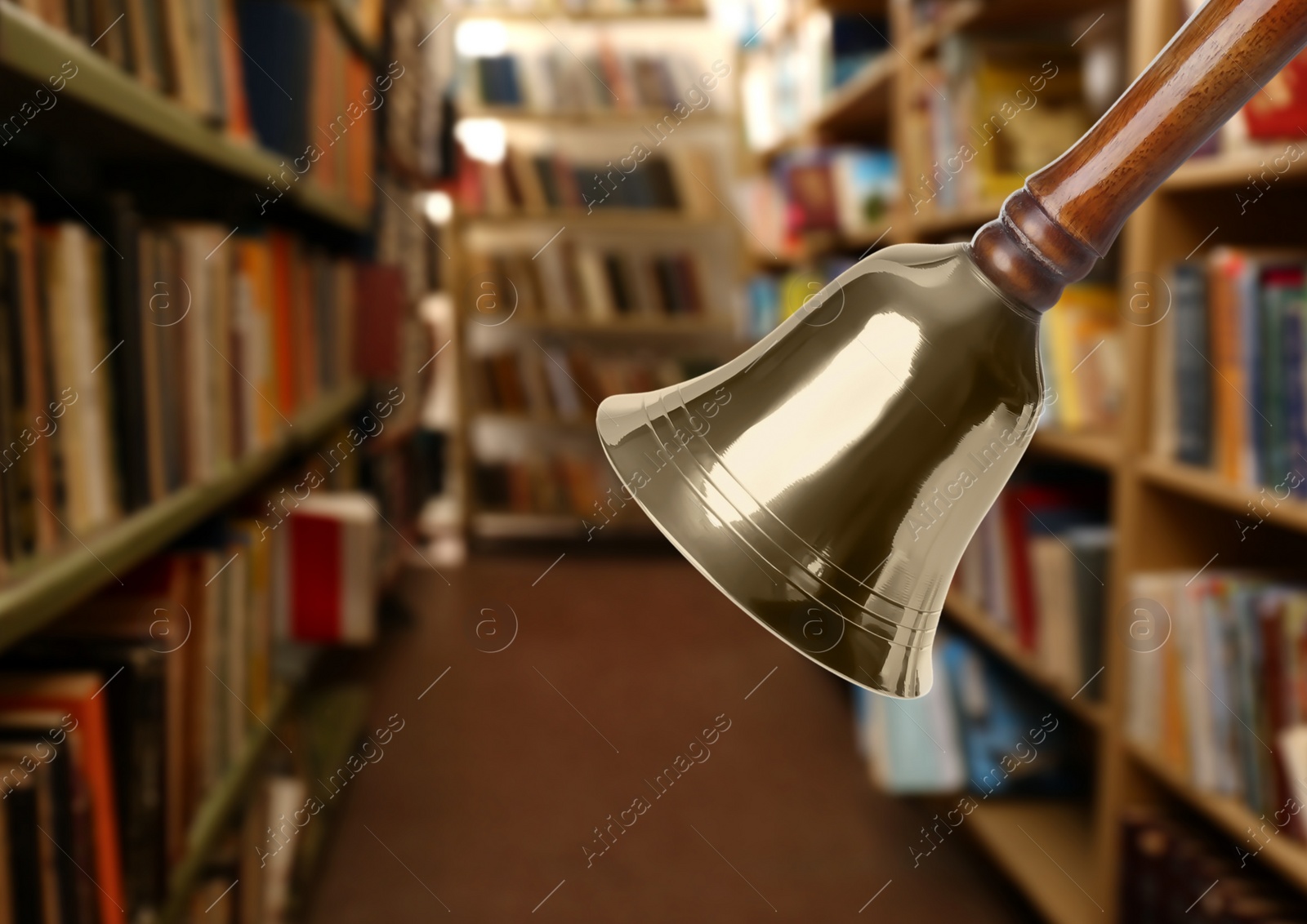 Image of Golden school bell with wooden handle and blurred view of books on shelves in library