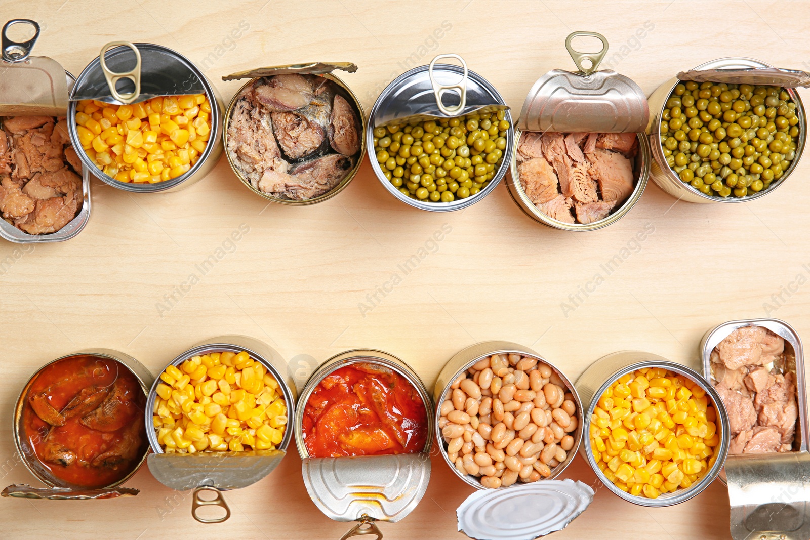 Photo of Open tin cans of conserved products on wooden table, flat lay with space for text