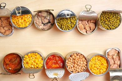 Open tin cans of conserved products on wooden table, flat lay with space for text