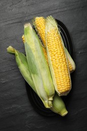 Photo of Fresh raw corn cobs on black table, top view