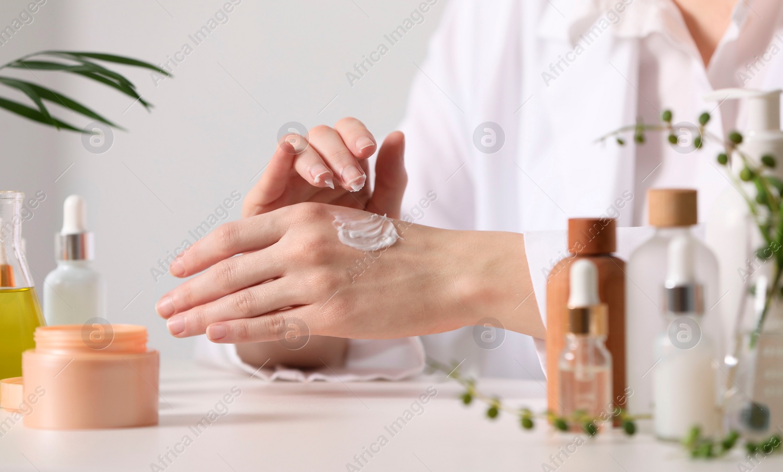 Photo of Dermatologist applying cream onto hand at white table indoors, selective focus. Testing cosmetic product