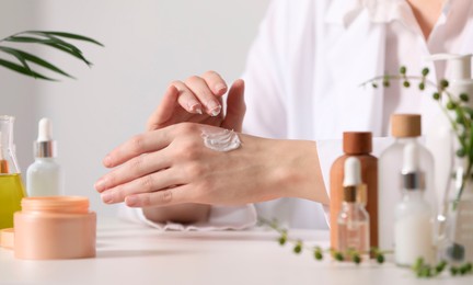 Photo of Dermatologist applying cream onto hand at white table indoors, selective focus. Testing cosmetic product