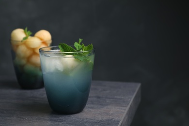 Glass with tasty melon ball drink on table against dark background. Space for text