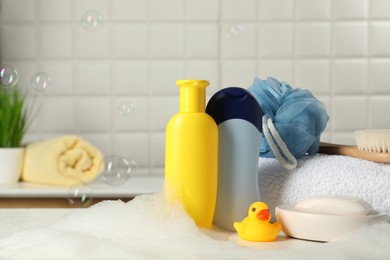Baby cosmetic products, bath duck, brush and towel on white table against soap bubbles. Space for text
