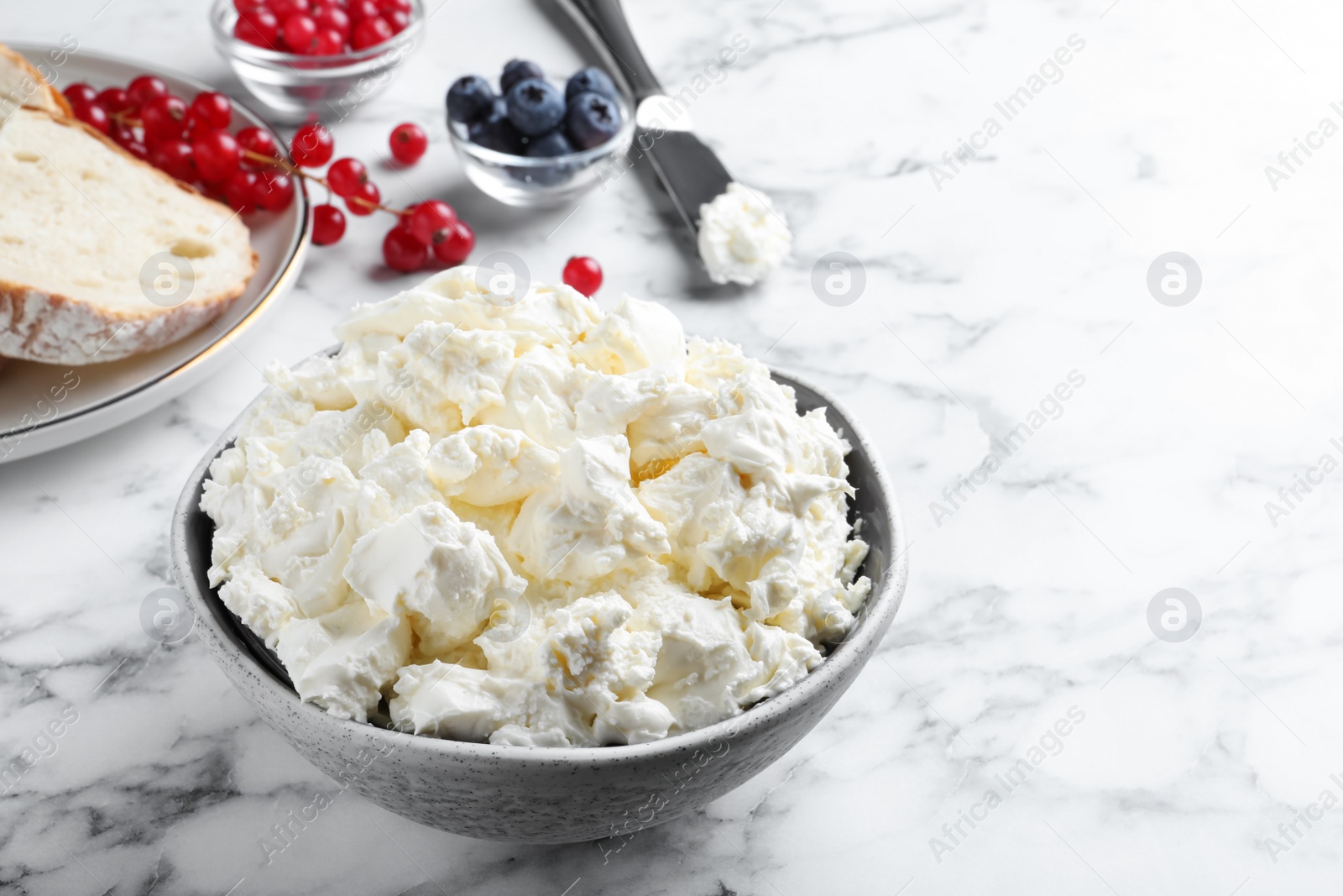 Photo of Tasty cream cheese and fresh berries on white marble table