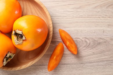 Photo of Delicious ripe persimmons on light wooden table, top view. Space for text