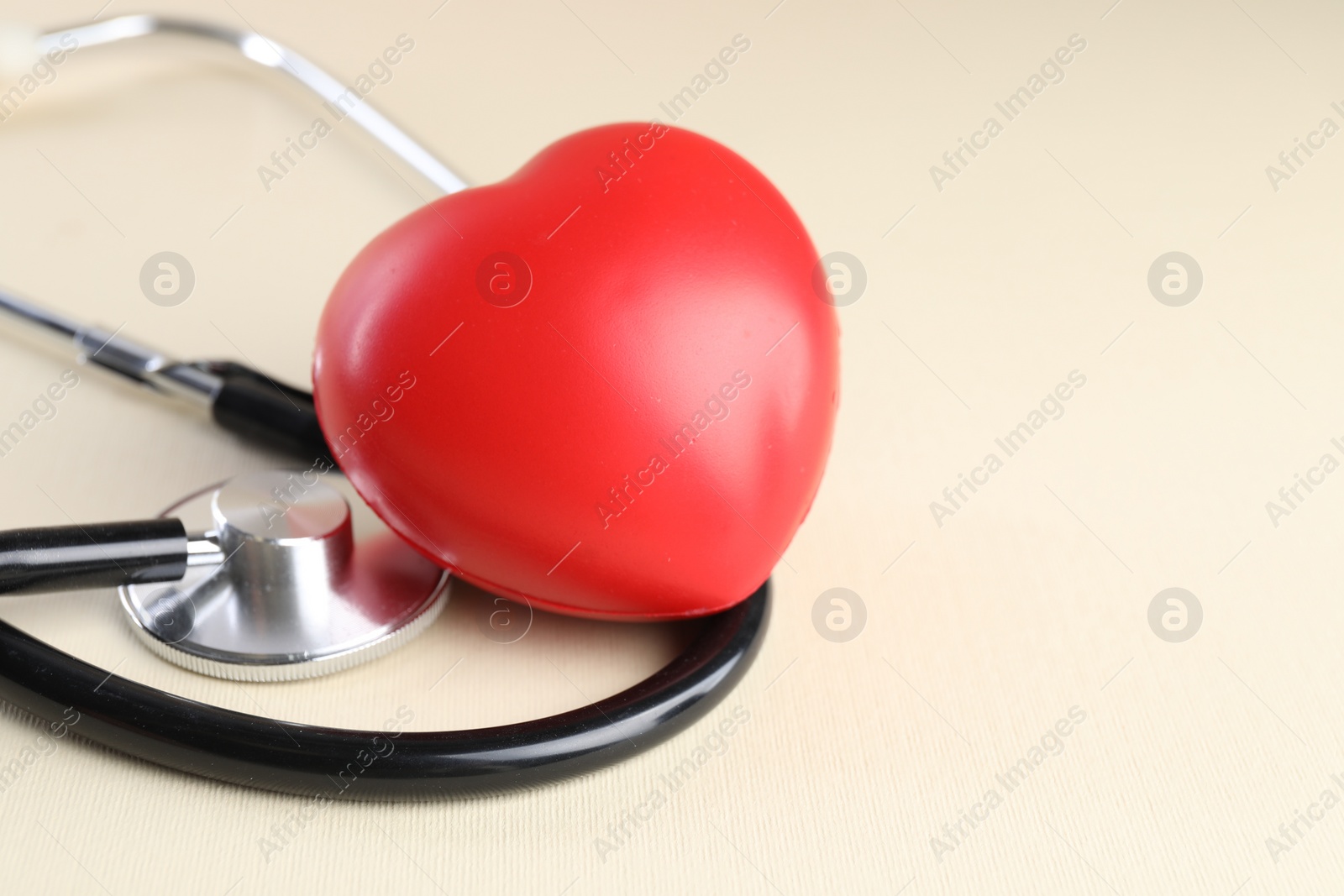 Photo of Stethoscope and red heart on beige background, closeup. Space for text