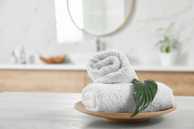 Photo of Rolled fresh towels and green leaf on white table in bathroom. Space for text