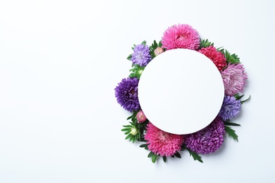 Beautiful aster flowers with sheet of paper on white background, top view. Space for text