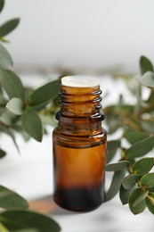 Bottle of eucalyptus essential oil and plant branches on white table, closeup