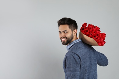 Photo of Happy man with red tulip bouquet on light grey background, space for text. 8th of March celebration