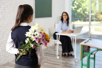Photo of Schoolgirl with bouquet congratulating her pedagogue in classroom. Teacher's day