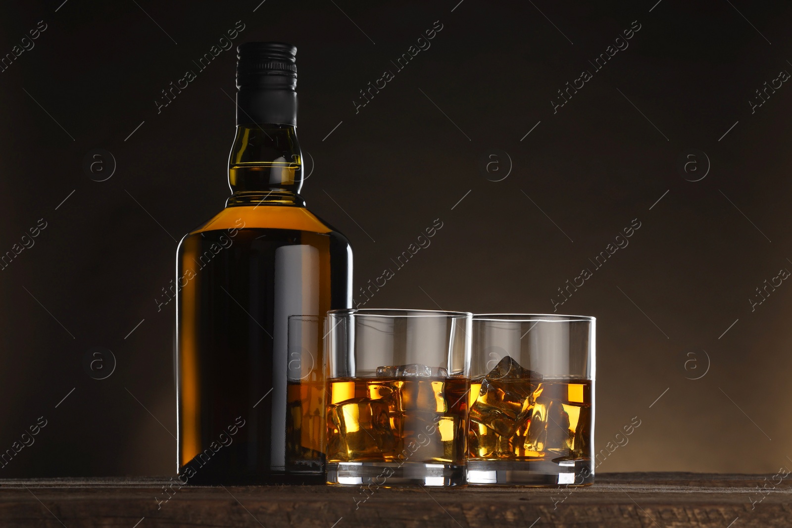 Photo of Whiskey with ice cubes in glasses and bottle on wooden table