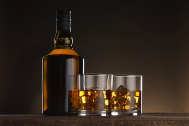 Photo of Whiskey with ice cubes in glasses and bottle on wooden table