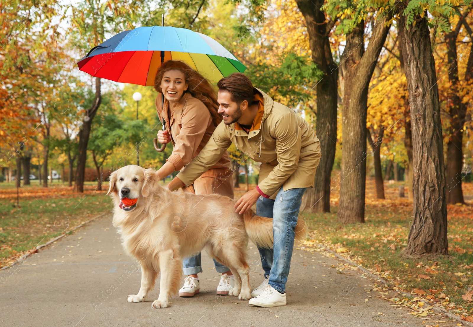 Photo of Young couple with umbrella and dog walking in park