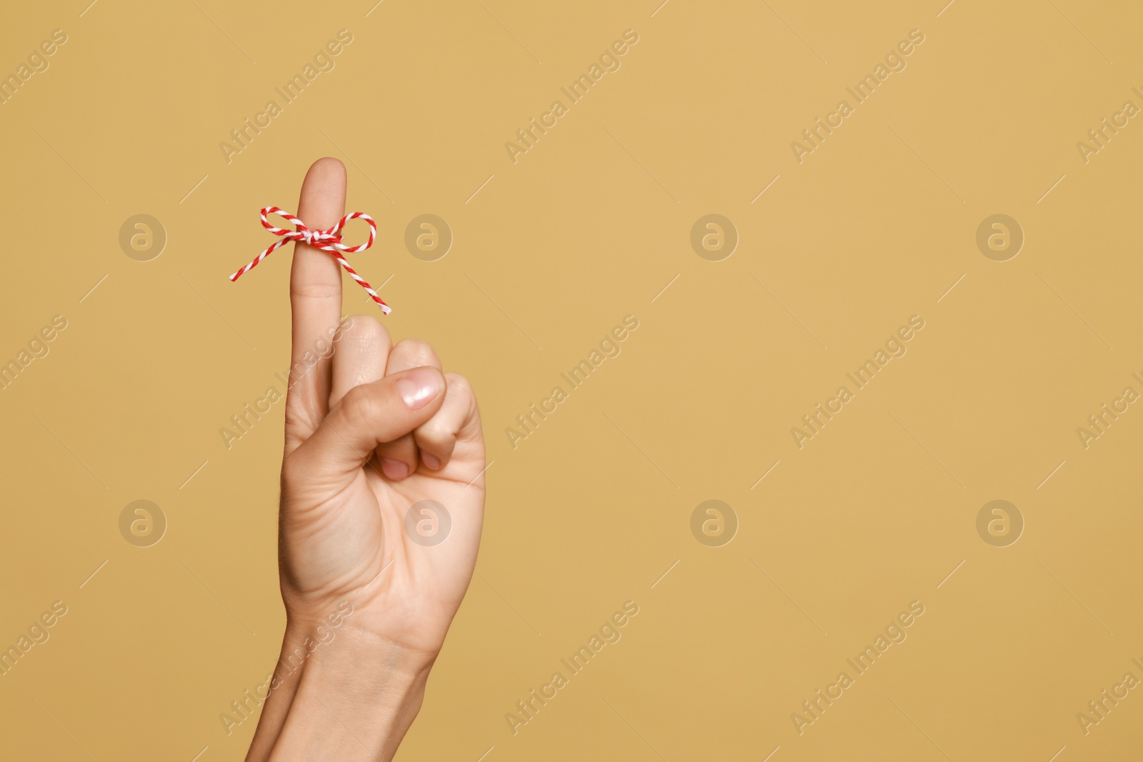 Photo of Woman showing index finger with tied bow as reminder on light brown background, closeup. Space for text