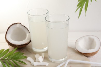 Photo of Glasses of coconut water, palm leaves and nuts on white table